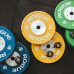 Colorful Rogue weight plates arranged on a gym floor visualizing fitness and strength.