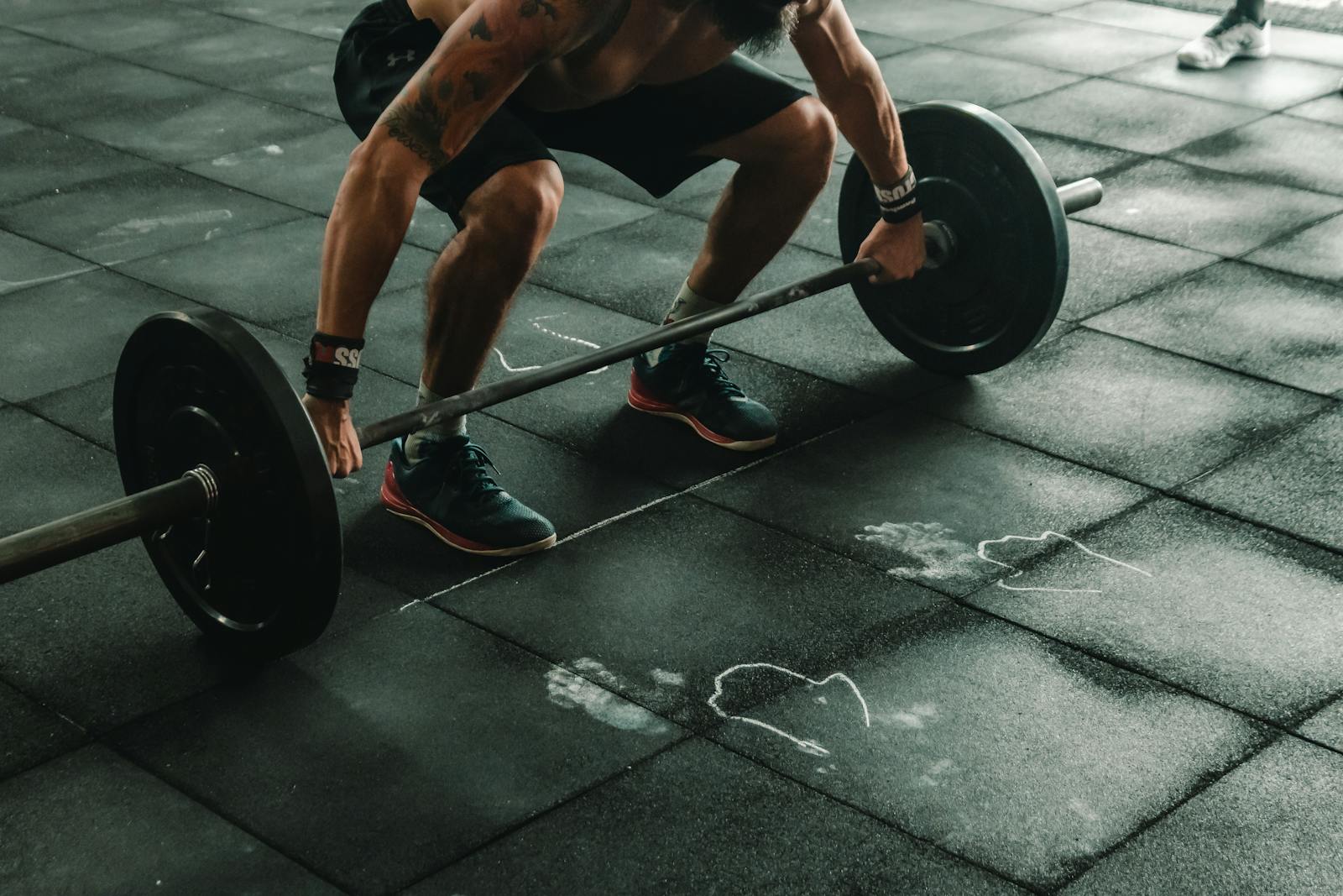 A muscular man in a gym preparing to lift a heavy barbell, showcasing strength and fitness.