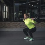 Dedicated woman in neon activewear performs a weighted squat in an indoor gym setting.