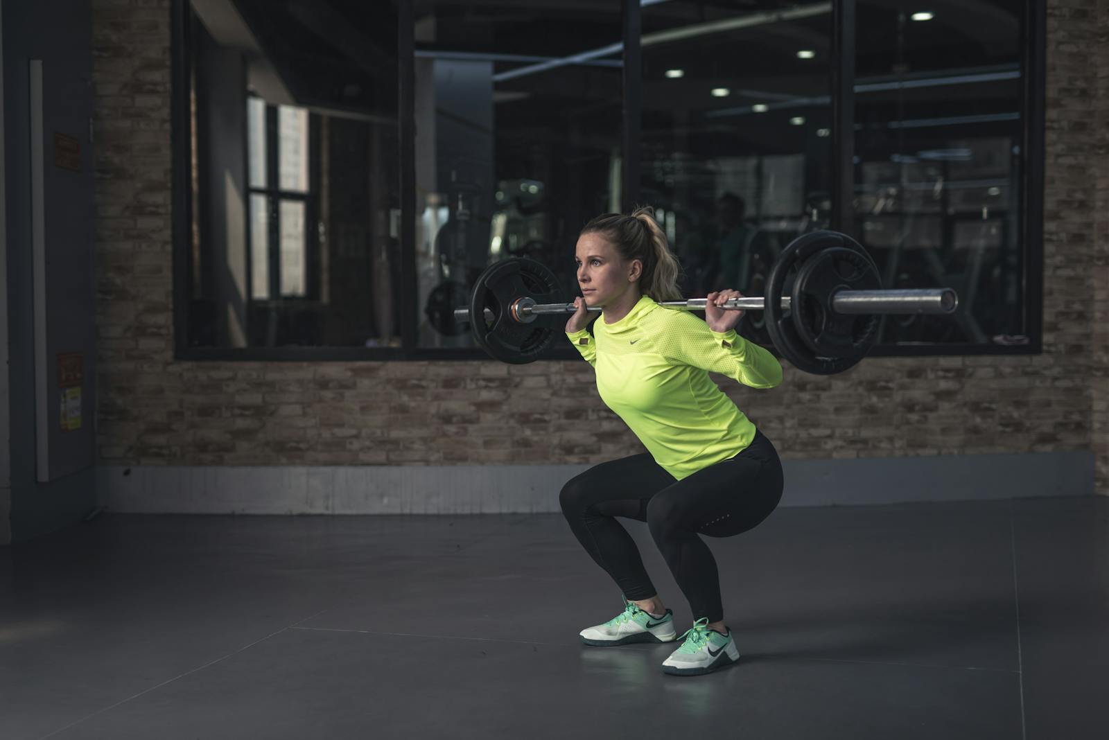 Dedicated woman in neon activewear performs a weighted squat in an indoor gym setting.