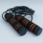 A minimalist close-up of black and orange exercise skipping rope on a clean white background.