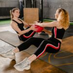 Two women exercising with a medicine ball in a gym setting, promoting fitness and well-being.