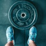 Blue sneakers next to a weight plate on a gym floor, top view.