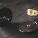 A heavy barbell and weightlifting belt on a gym floor, emphasizing strength and fitness.