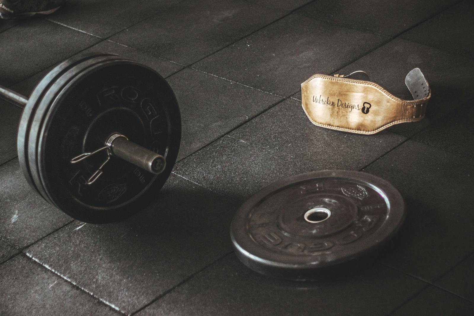 A heavy barbell and weightlifting belt on a gym floor, emphasizing strength and fitness.