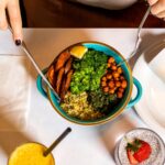 person holding silver spoon and blue ceramic bowl with food