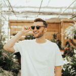 man in white crew-neck shirt wearing sunglasses standing near plants