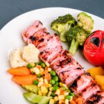 grilled meat with green vegetable and red chili on white ceramic plate